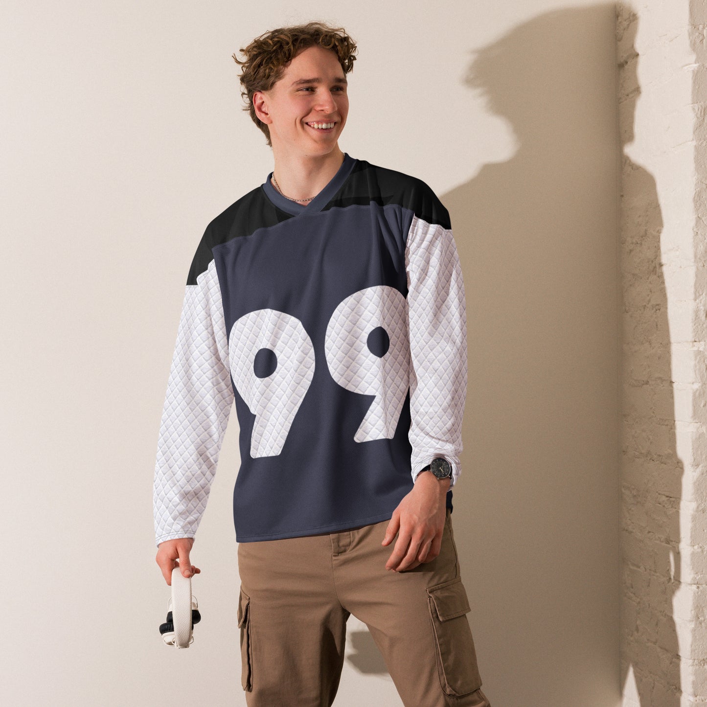 Hockey jersey featuring a large number 99 on the front in white with a unique quilted design texture on the shoulders and sleeves, against a navy backdrop with a v-neck collar and black upper chest panel male model smiling