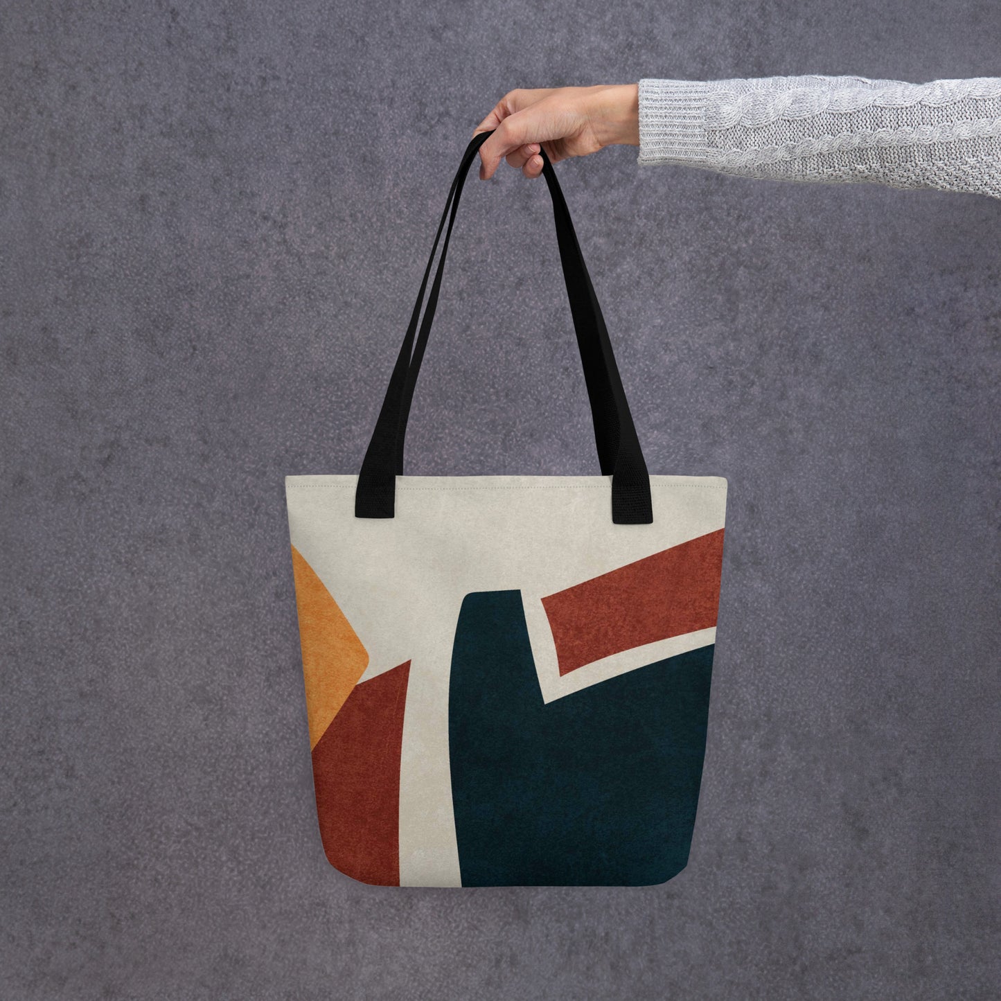 Person holding a HFT Tote Bag IV with abstract geometric design, showcasing rich earth tones setup against a textured gray background.