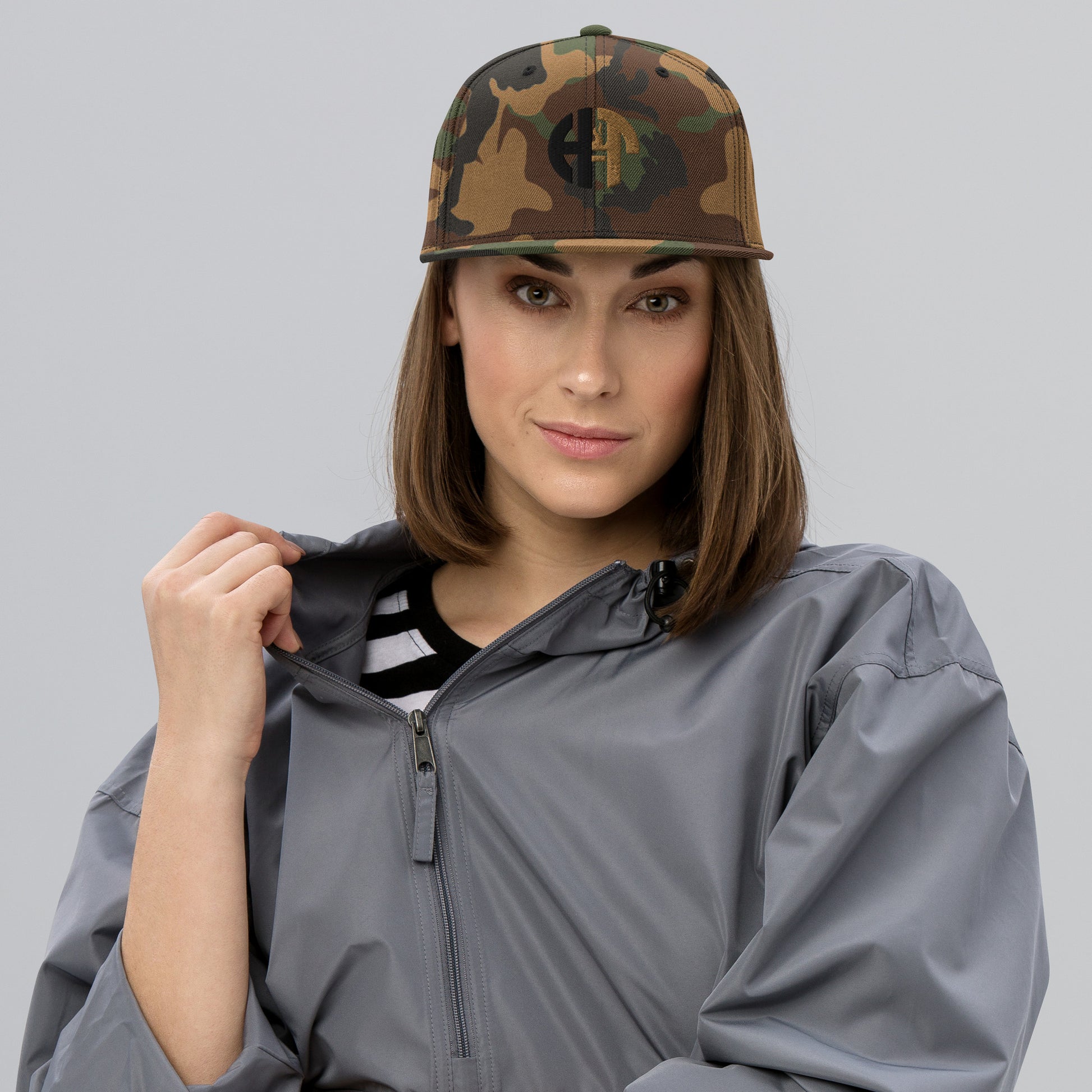 A stylish two-tone hat with a classic fit, featuring a structured green camo-colored crown with a flat brim and full buckram for added durability. The front displays an embroidered 'HFT' logo in black and gold, and the hat is topped with a black button. An adjustable snap closure at the back provides a comfortable and custom fit for most head sizes female