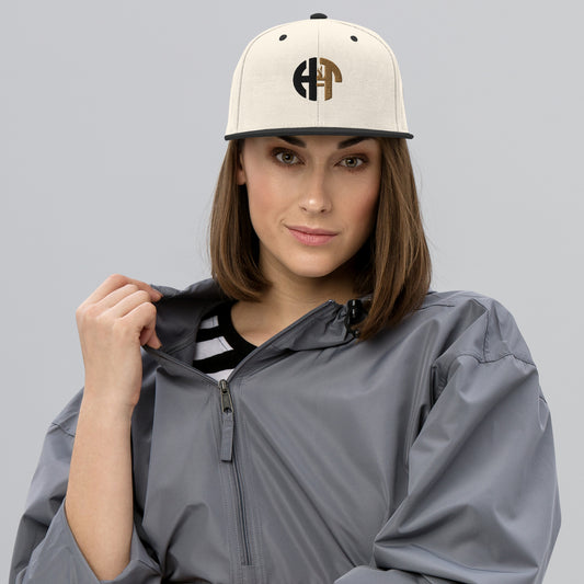 A stylish two-tone hat with a classic fit, featuring a structured cream-colored crown with a flat black brim and full buckram for added durability. The front displays an embroidered 'HFT' logo in black and gold, and the hat is topped with a black button. An adjustable snap closure at the back provides a comfortable and custom fit for most head sizes female