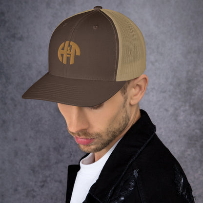 A stylish six-panel trucker cap with a breathable mesh back and a front panel featuring a black 'HFT' logo, complete with a pre-curved brim and an adjustable snap closure for comfort khaki left