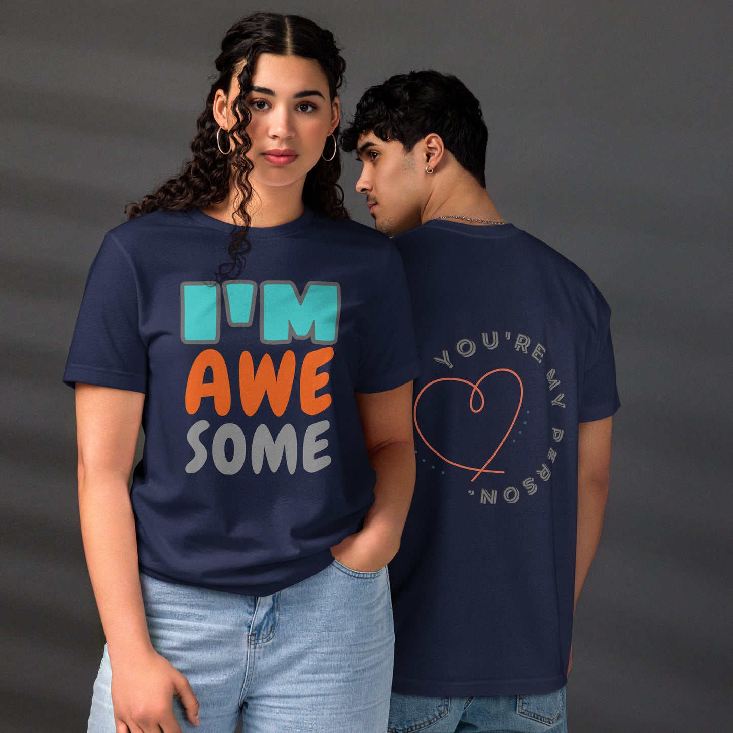 Couple wearing HFT Unisex Staple Eco T-shirts, with the man’s navy tee featuring the text 'you're my person' inside a red heart and the woman's navy tee with the text 'I'm awesome' in multicolor