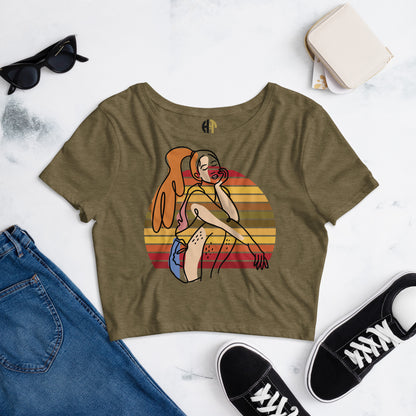  Heather Olive HFT Women's Crop Tee with a colorful, retro-inspired graphic print of a woman seated and wearing headphones, displayed on a flat surface